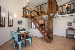 Un coin repas avec un escalier en bois, des chaises turquoise et une table sur laquelle se trouve un saladier.