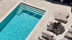 Una piscina rectangular con agua cristalina, rodeada de sillas de descanso y sombrillas.