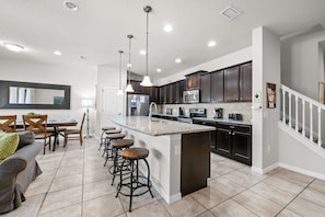 A modern kitchen with dark cabinets, a central island, bar stools, and a dining area with a table and chairs.