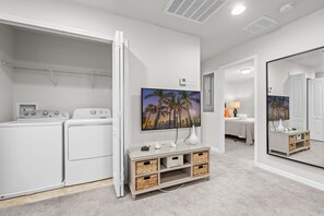 A laundry room with a washing machine, dryer, and a television on a glass cabinet. - South Private Splash Pool • Lazy River • Resort Pool • 15 Minutes to Disney (Kissimmee)