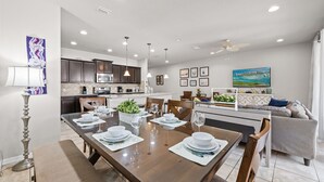 A modern kitchen with dark cabinets, a dining area with a long table set for four, and a ceiling fan. - South Private Splash Pool • Lazy River • Resort Pool • 15 Minutes to Disney (Kissimmee)