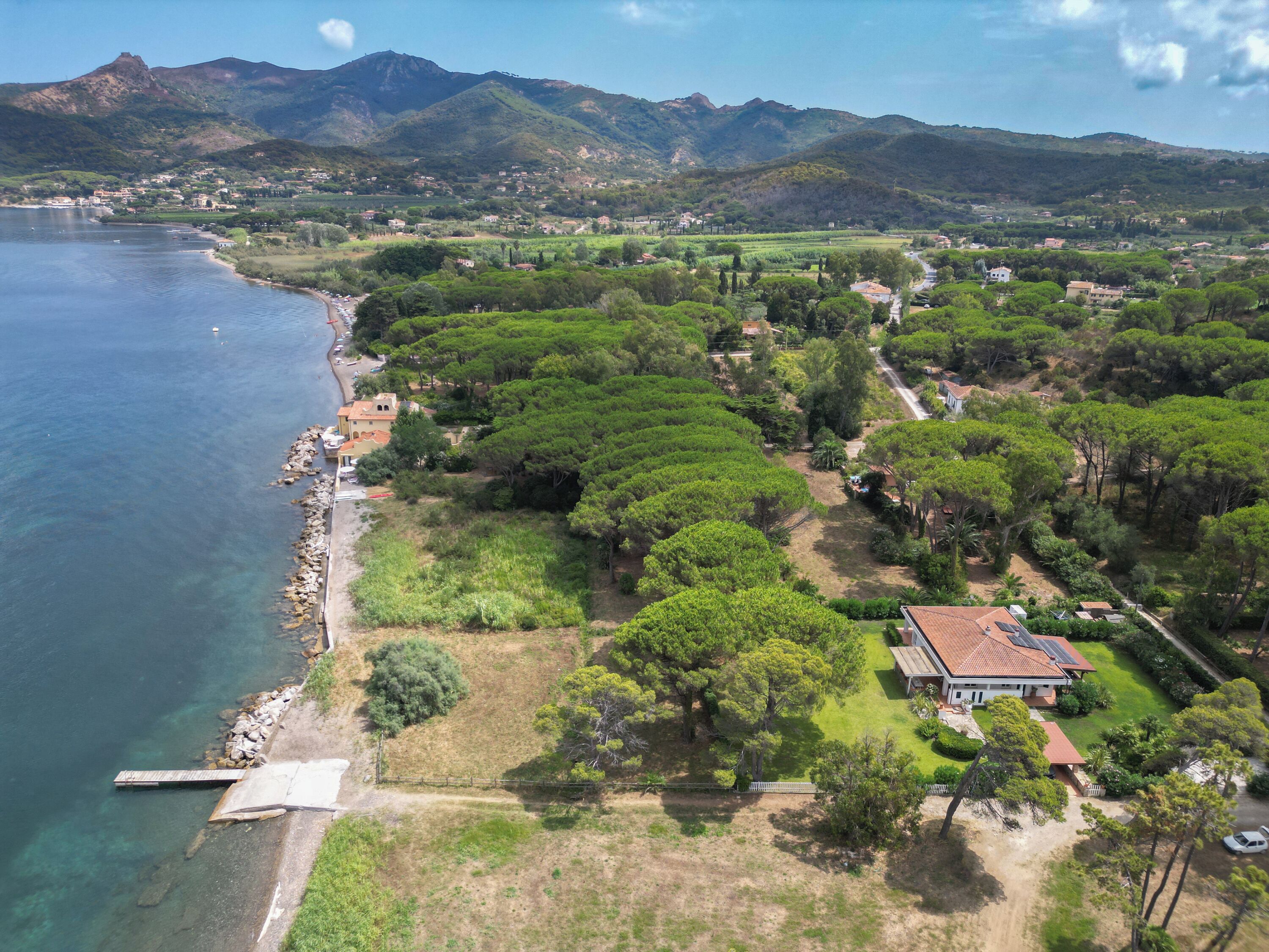 A coastal property with a dock, a house with a red roof, and a mountainous backdrop.