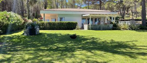 A modern two-story house with a covered patio, surrounded by a well-maintained lawn and dense trees.