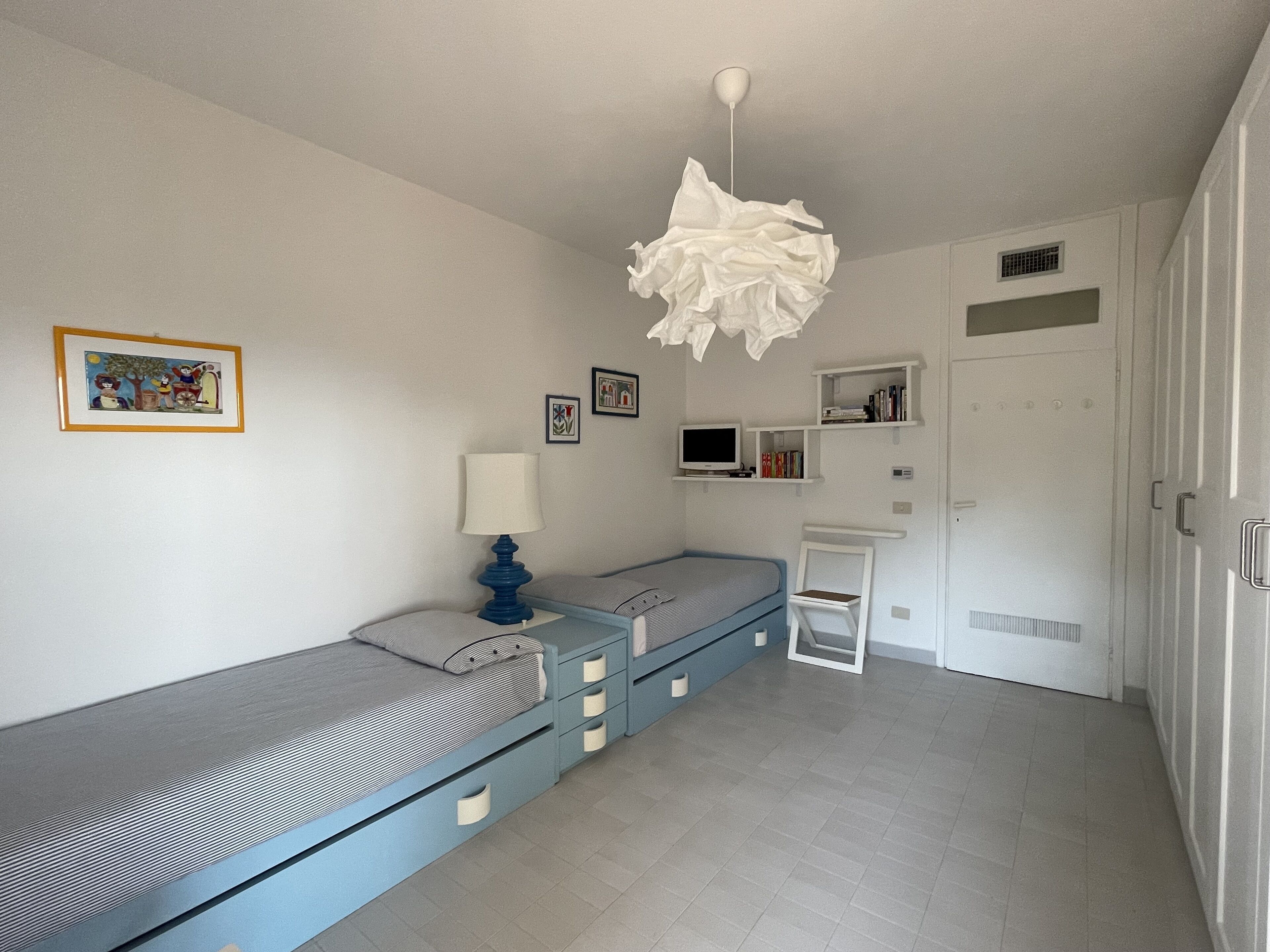 Quarto com cama, mesa de cabeceira, luminária e televisão na parede.