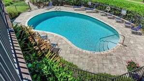 A swimming pool with a curved edge, surrounded by a paved deck and lounge chairs. - Sea Grape Inn #2- Beachfront Property (Longboat Key)