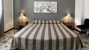 A bedroom with a striped bedspread, two bedside lamps, a wall-mounted air conditioner, and a floral-patterned floor. - Villa Gelvi. Apartment in villa 2 minutes from the sea (wi fi, solarium, games) (Castellammare del Golfo)