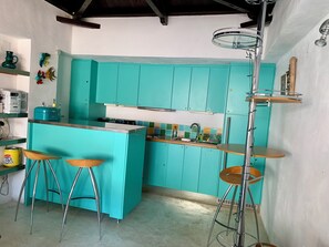 A kitchen with teal cabinets, a central island with stools, and a high ceiling with exposed beams.