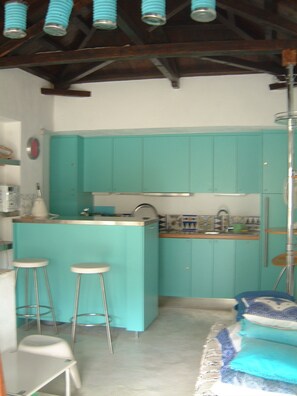 A compact kitchen with teal cabinets, a small island, stools, and a sink.