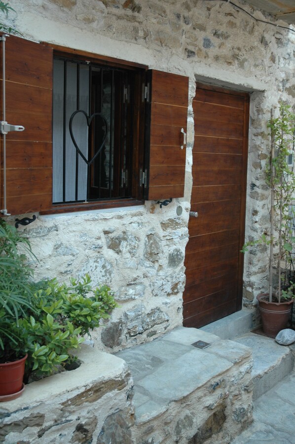 A stone building with a wooden door and window, potted plants, and stone steps.