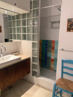 Een badkamer met een wit wastafel, houten wastafelmeubel, een douchecabine met glazen wanden en een douchegedeelte met kleurrijke tegels.