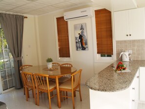 Un coin repas avec une table et des chaises, une cuisine avec un plan de travail et des placards, et une fenêtre avec des stores.