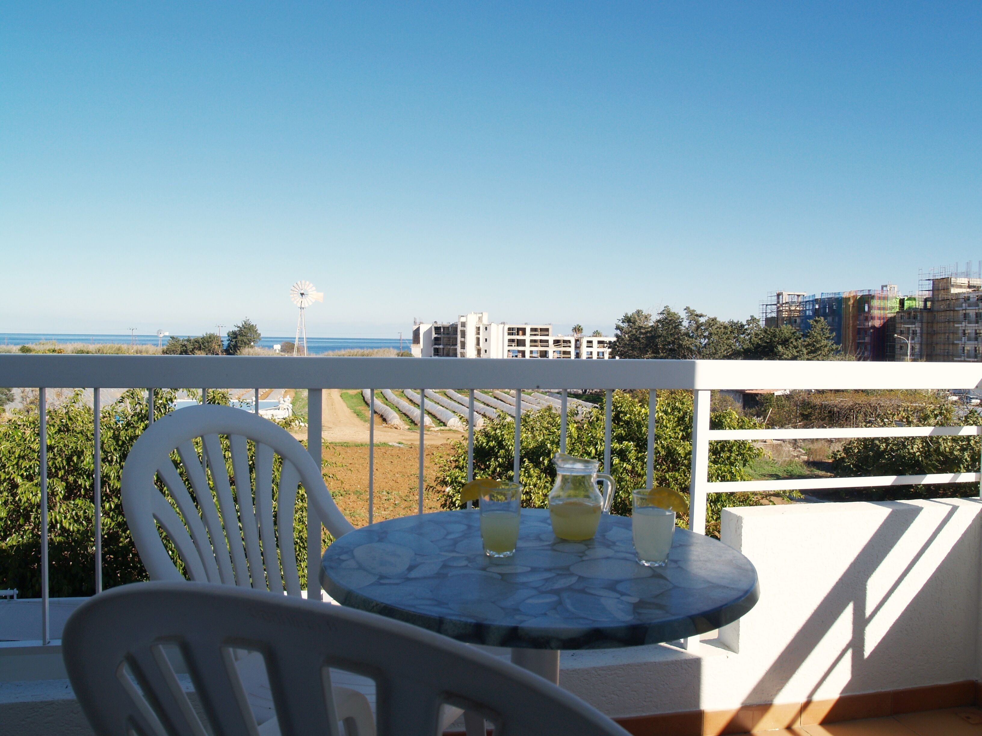A balcony with a table and chairs, overlooking a coastal view with buildings and a windmill.
