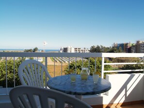A balcony with a table and chairs, overlooking a beach and buildings.