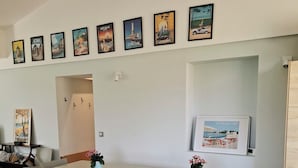 A dining area with a long table and six chairs, framed artwork on the wall, and a bookshelf with books and a small plant. - Architect-designed villa for 8 people close to the beach (Saint-Palais-Sur-Mer)