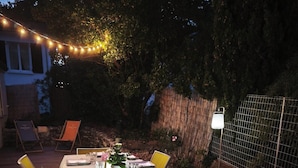 An outdoor dining area with a table set for four, surrounded by chairs, under string lights. - Architect-designed villa for 8 people close to the beach (Saint-Palais-Sur-Mer)