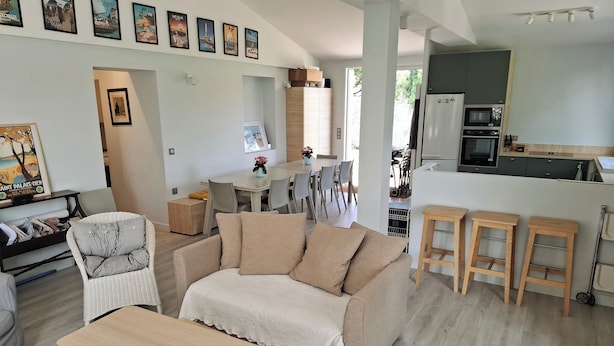 A modern living room with a beige sofa, a wooden coffee table, and a dining area with a white table and chairs. - Architect-designed villa for 8 people close to the beach (Saint-Palais-Sur-Mer)