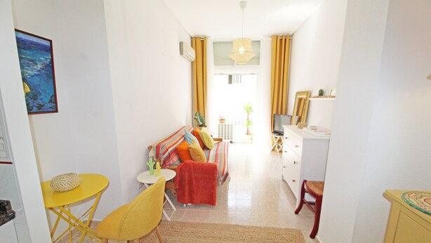 Un espacio habitable compacto con sofá, una pequeña mesa de comedor, una silla y una kitchenette.
