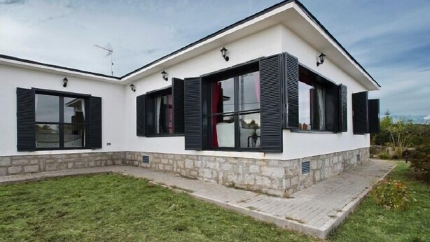 Een modern huis met twee verdiepingen, een stenen fundering, grote ramen met zwarte luiken en een kleine voortuin.