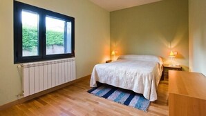 Een slaapkamer met een groot raam, een bed, twee bedlampen, een radiator en een houten bureau.