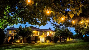 Uma casa de dois andares com uma entrada bem iluminada, cercada por um gramado e árvores.