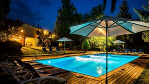 Piscina com espreguiçadeiras e guarda-sóis, cercada por um deck de madeira e árvores.