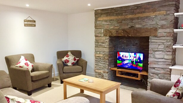 A living room with a stone fireplace, two armchairs with floral cushions, a wooden coffee table, and a television on a stone wall. - March Cottage Terraced Cottage Brecon Brecon Beacons Free Wifi  (Brecon)