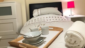 A neatly made bed with heart-patterned bedding, a bedside table with a lamp, and a tray with bowls, spoons, and a cup. - March Cottage Terraced Cottage Brecon Brecon Beacons Free Wifi  (Brecon)