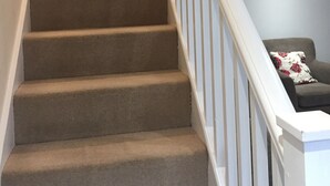 A carpeted staircase with white railings leading to a room with a blue wall and a chair with a floral pillow. - March Cottage Terraced Cottage Brecon Brecon Beacons Free Wifi  (Brecon)