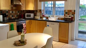 A modern kitchen with wooden cabinets, a microwave, a stove, and a dishwasher. There is a dining table with chairs and a window providing a view of the outside. - March Cottage Terraced Cottage Brecon Brecon Beacons Free Wifi  (Brecon)