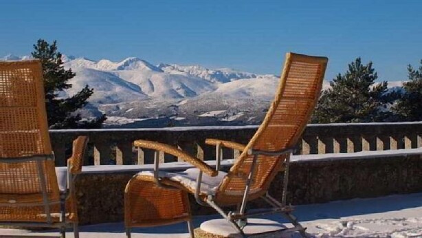 Sedie lounge in vimini su un balcone con vista su una montagna innevata.