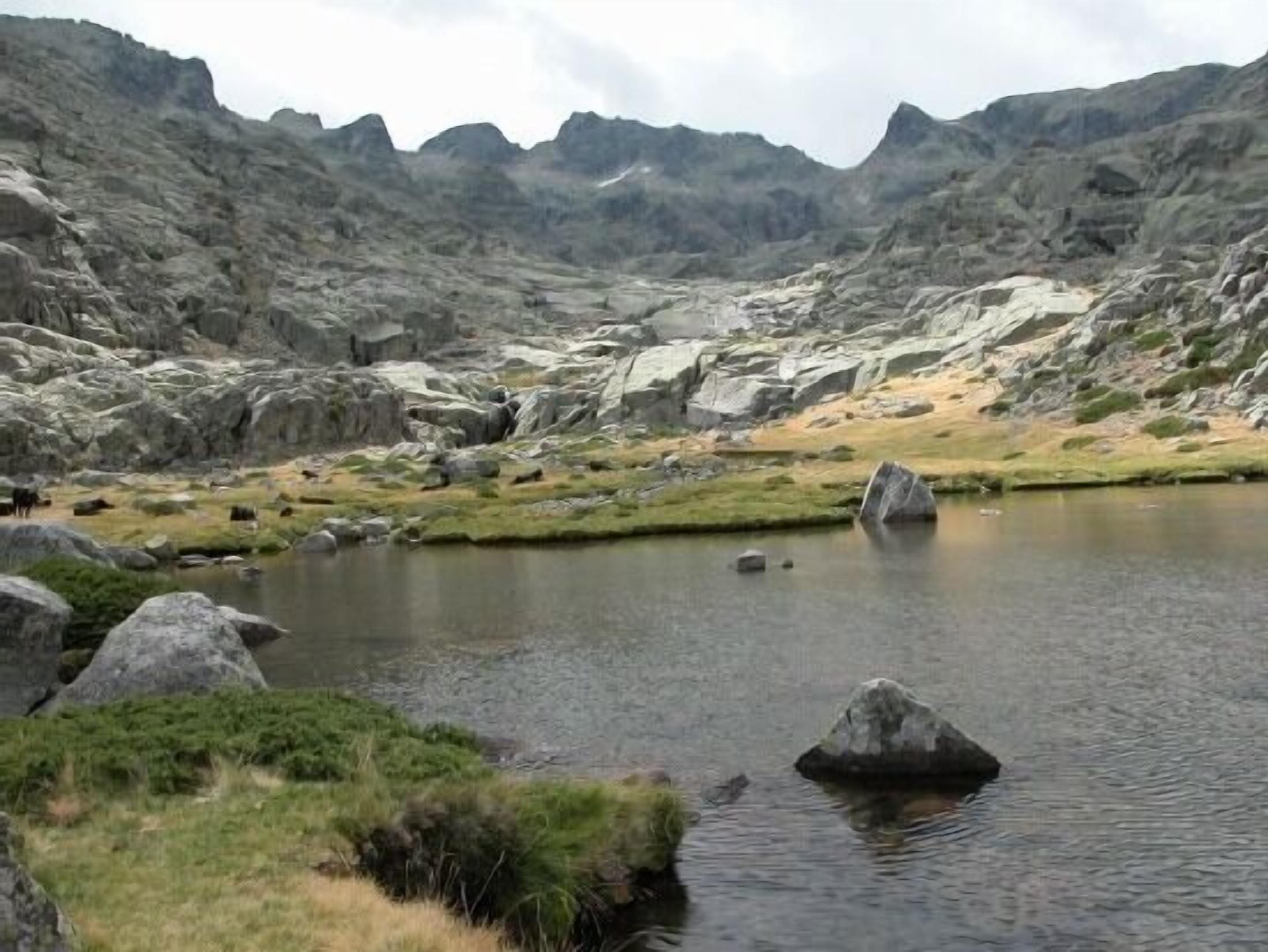 Eine Berglandschaft mit einem See, umgeben von Felsen und vereinzelter Vegetation.