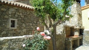 Un edificio in pietra con una piccola finestra, un albero con fiori rosa e un muro di pietra.