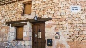 A rustic stone building with a wooden door and a sign reading "LA FUENTE DEL POVAL".