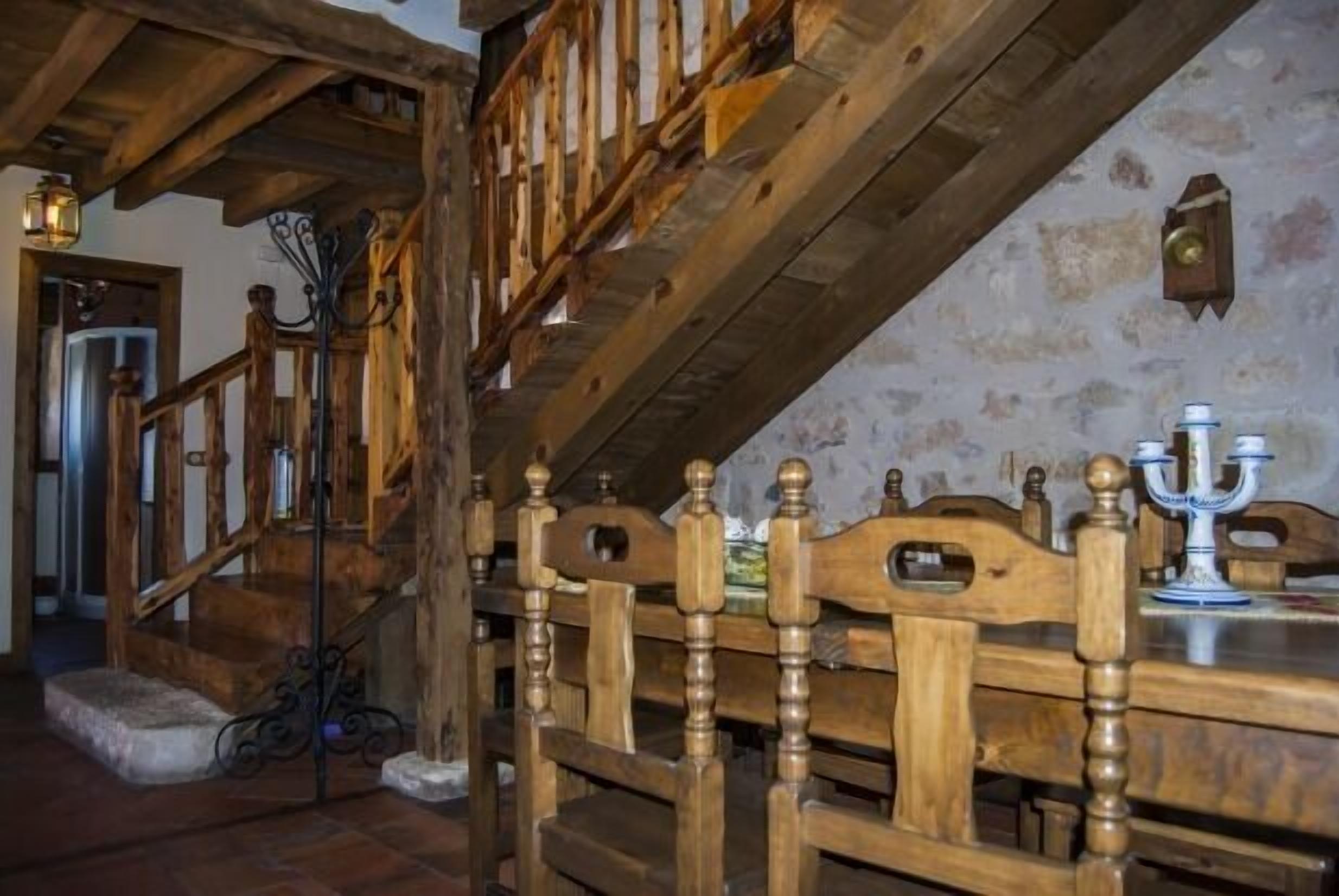 Una escalera de madera con diseño rústico, una mesa de comedor con candelabro y una pared de piedra al fondo.