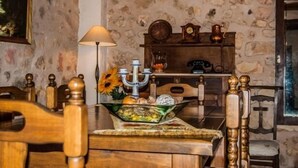 A rustic dining area with a stone wall, wooden furniture, and a table set with a candelabra, a vase with flowers, and a bowl of fruit.