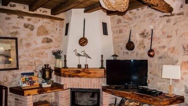 A rustic living room with a stone wall, a fireplace, a television, and wooden shelves.