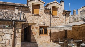 A stone building with a tiled roof, a small window with shutters, and a stone staircase leading to an entrance.