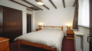 A bedroom with a wooden bed, two bedside tables with lamps, a wardrobe, and a window with curtains.