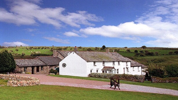 A white building with a traditional design, a stone pathway leading to it, and a grassy area with a bench.