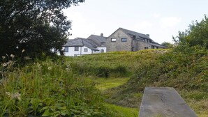 A stone house with a sloped roof, surrounded by lush greenery and a wooden bench.