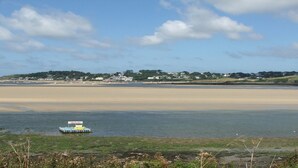 A coastal scene with a boat docked near the shore, a sandy beach, and a distant town with houses.