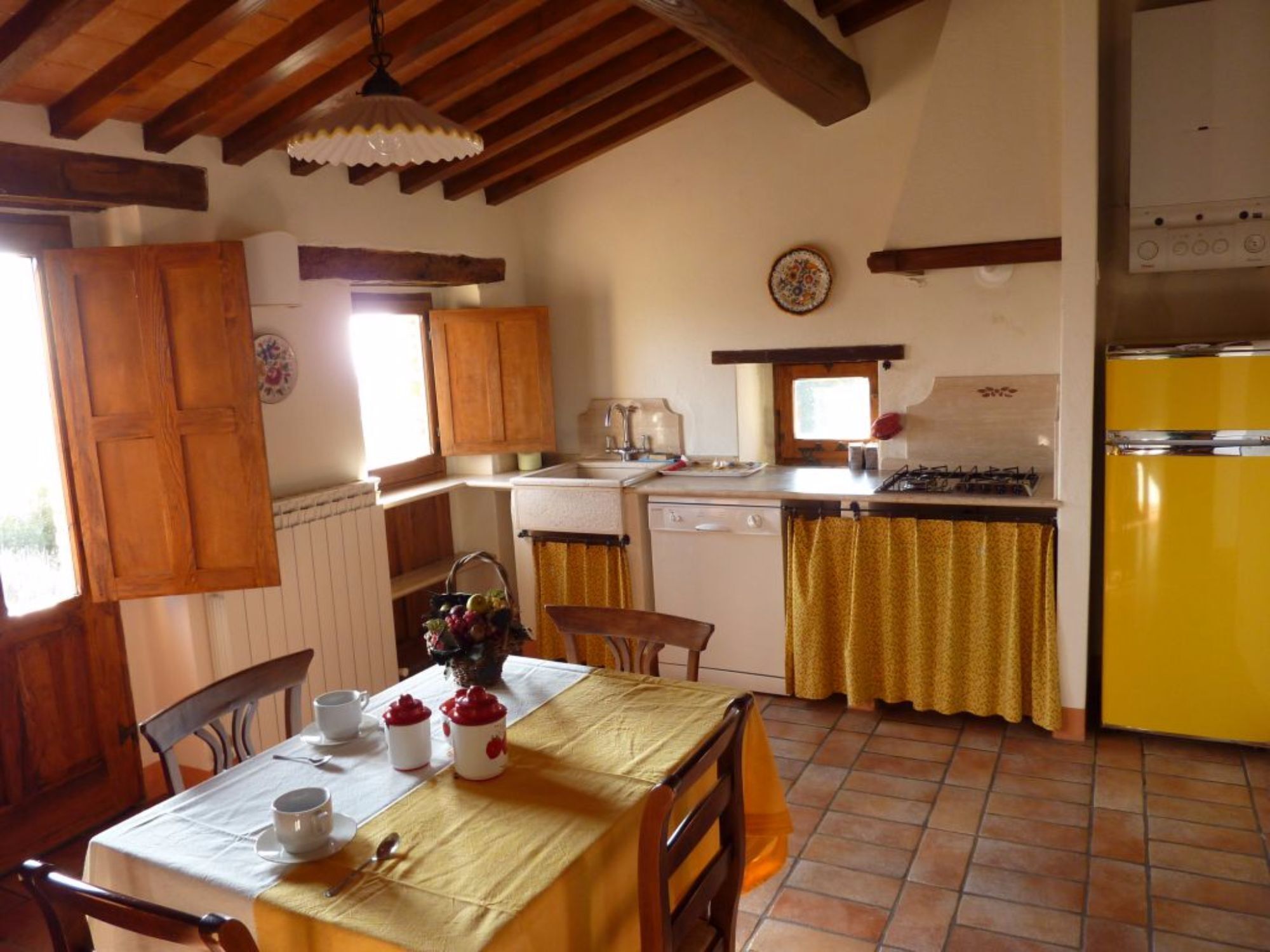 Une cuisine rustique avec des meubles de rangement en bois, un réfrigérateur jaune et un coin repas avec une table mise pour deux personnes.