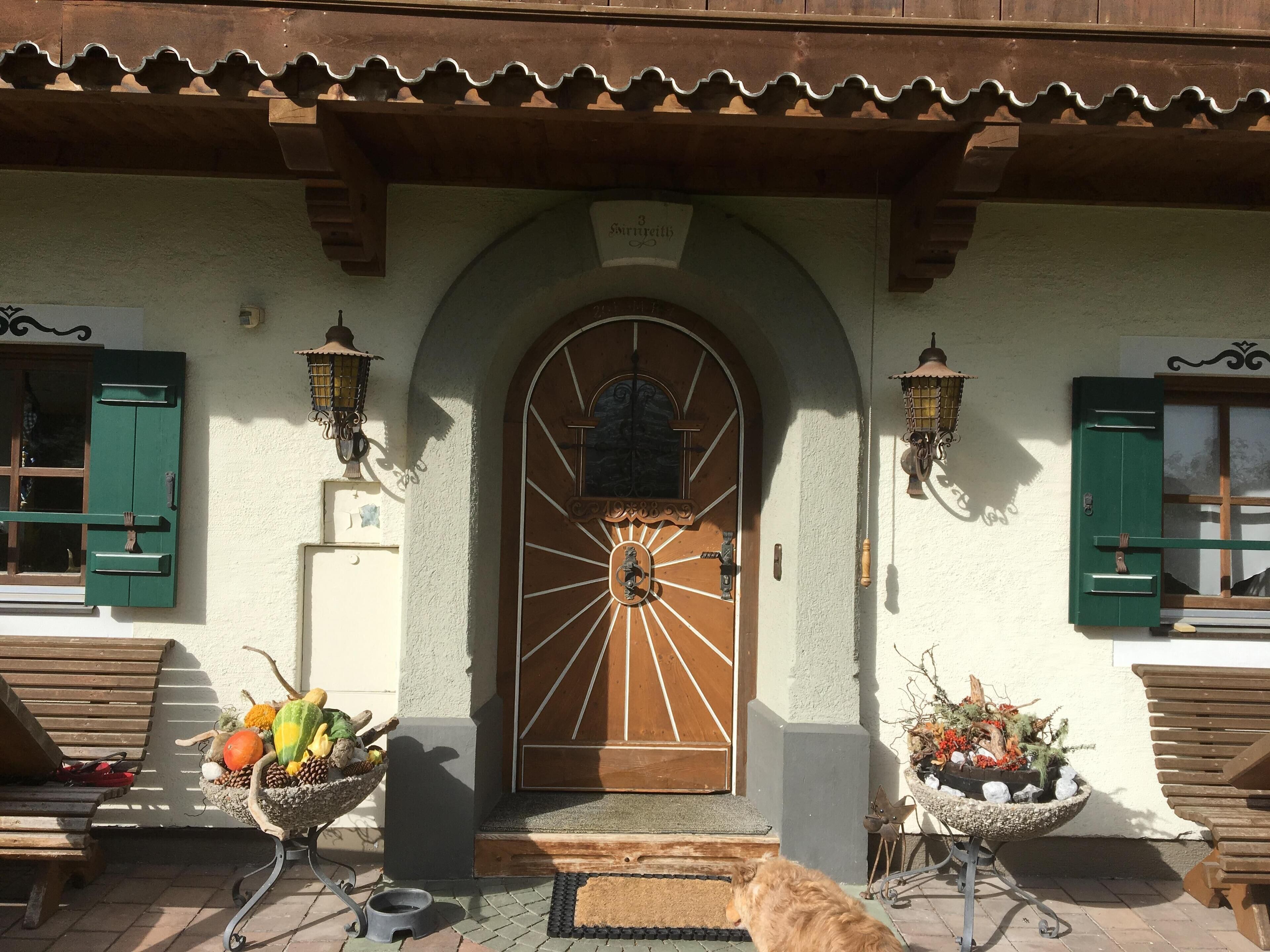 A traditional building with a central arched entrance, wooden shutters, and two wall-mounted lanterns.
