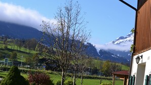 Un paysage de montagne avec un ciel dégagé, un arbre au premier plan et un bâtiment doté d’un balcon.