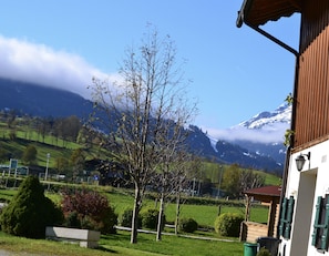 Eine Berglandschaft mit blauem Himmel, einem Baum im Vordergrund und einem Gebäude mit Balkon.