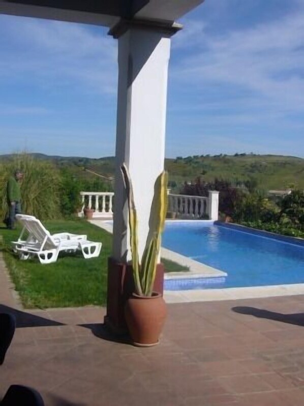 Un espace piscine avec vue sur les collines, une chaise longue blanche et une plante en pot.