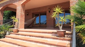 A brick building with a covered patio, steps leading to a door, and potted plants.
