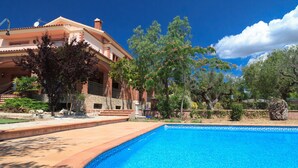 A large house with a swimming pool, surrounded by trees and a clear blue sky.