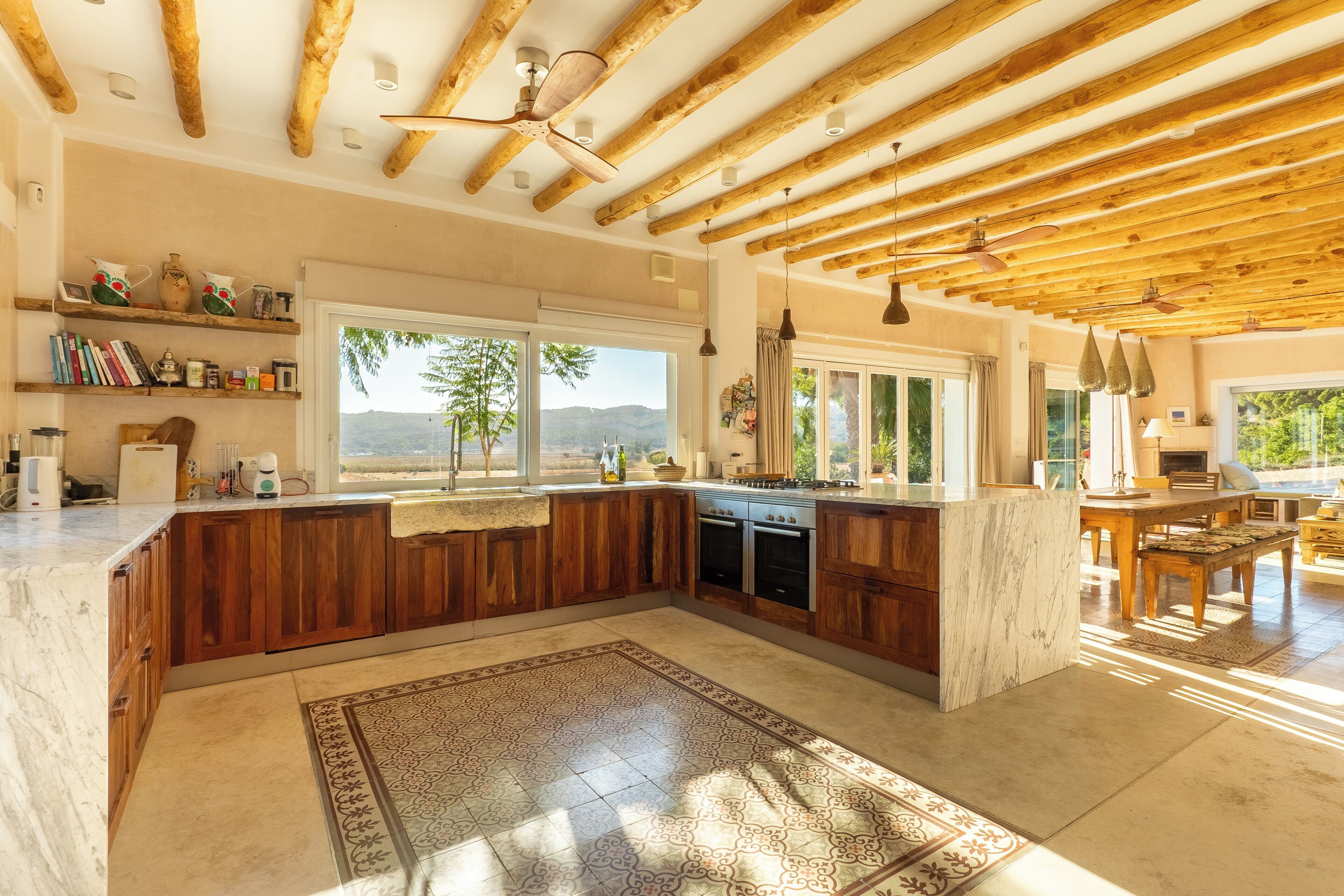 A spacious kitchen with wooden beams, a large island, and a view of the outdoors.