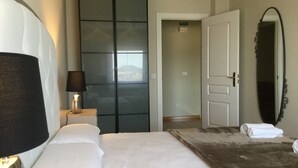 Ein Hotelzimmer mit Bett, Nachttischlampe, Kleiderschrank, Spiegel und einer Tür zu einem anderen Raum.
